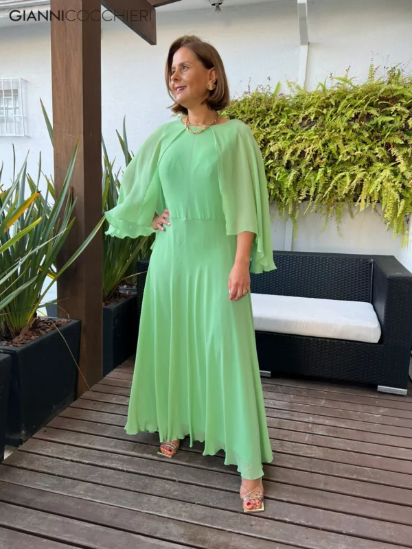 Vestido verde claro com tecido leve até o tornozelo. Manga estilo capa com o mesmo tecido.